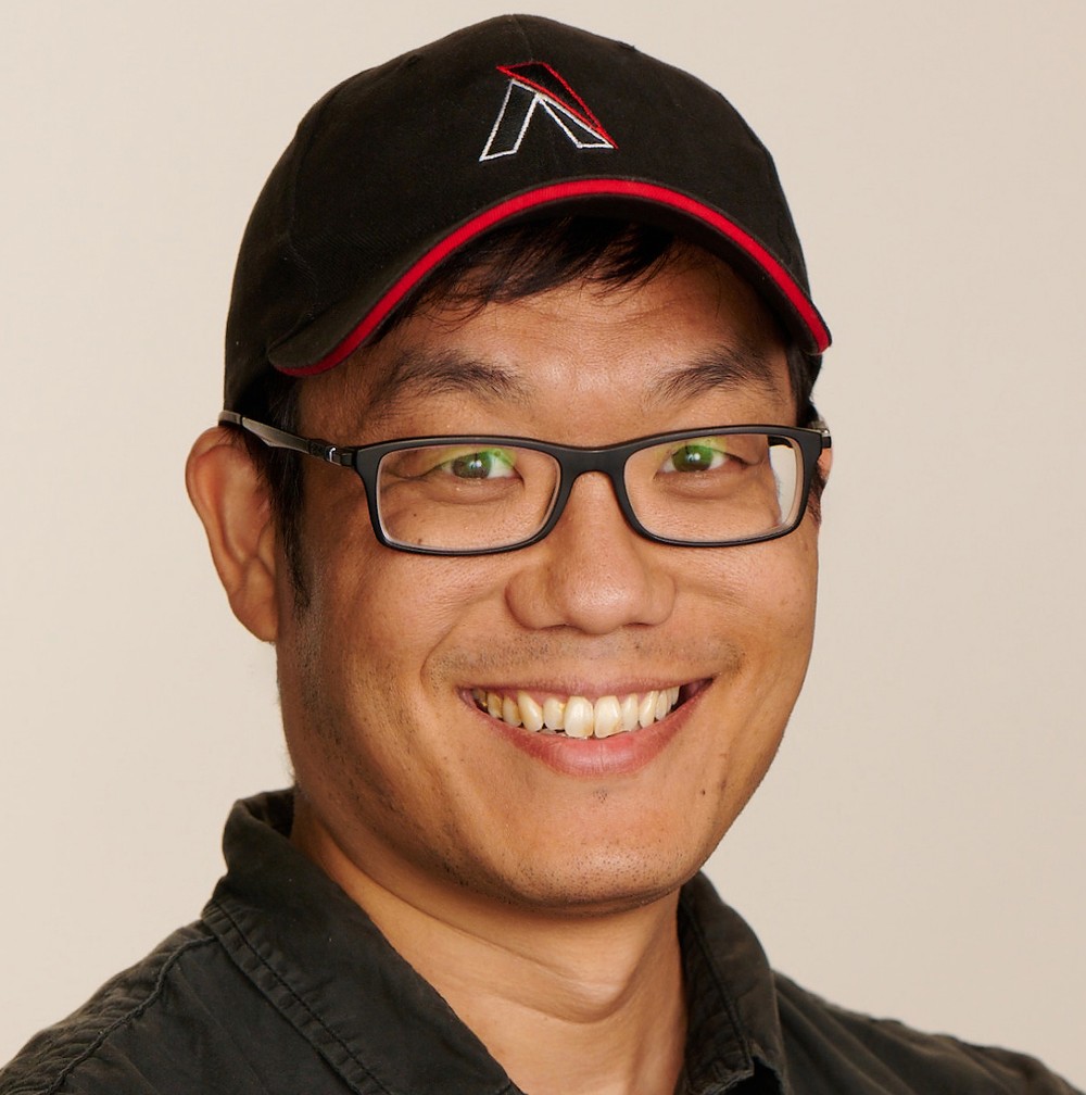 A man wearing large square glasses and baseball hat with an aputure logo on it